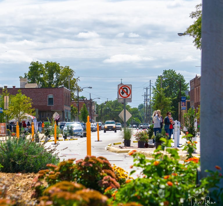 Urban street scene featuring temporary planters, traffic barriers, and pedestrians during a community event.