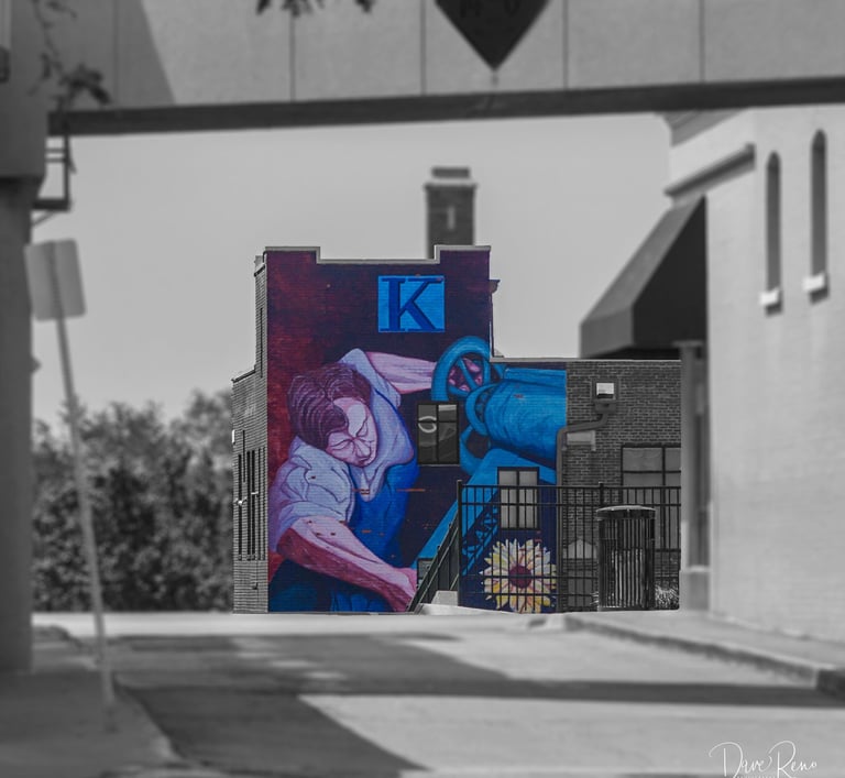 Urban mural of a labor figure on the Kansan Building, with selective color against a grayscale streetscape.