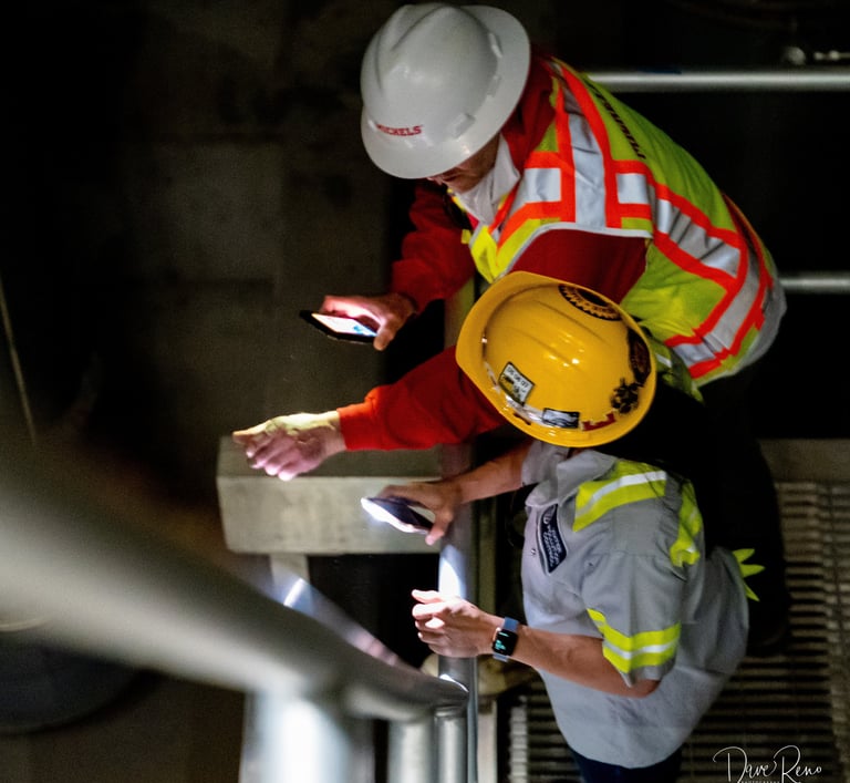Rep. Sharice Davids and a worker inspect equipment inside a flood pump station using phone lights.