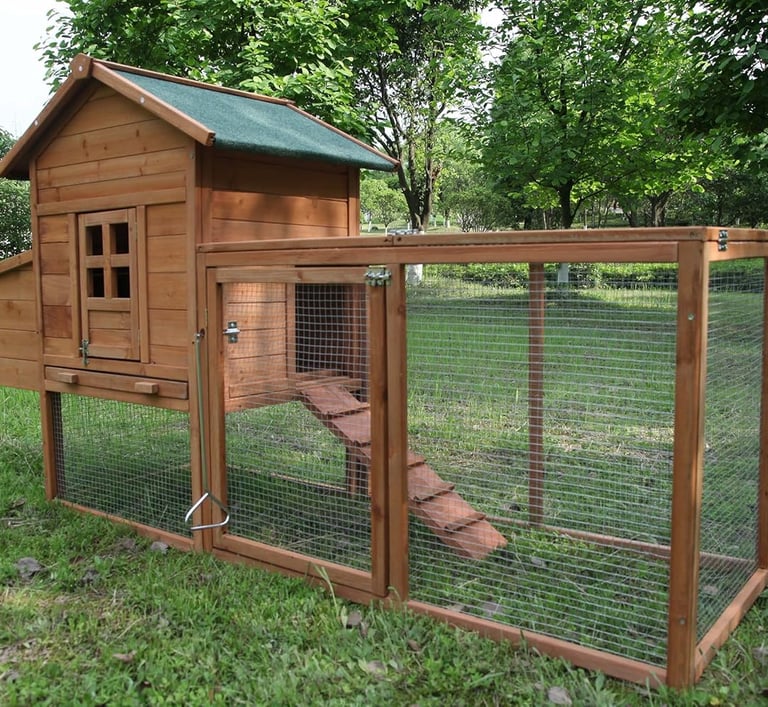 A wooden chicken coop with an outdoor wire mesh run and ramp on a green backyard lawn.