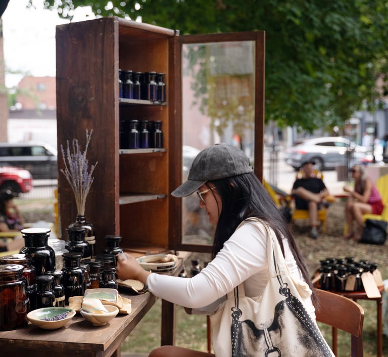 A woman wearing a baseball cap sits at a table in a park participating in an art installation