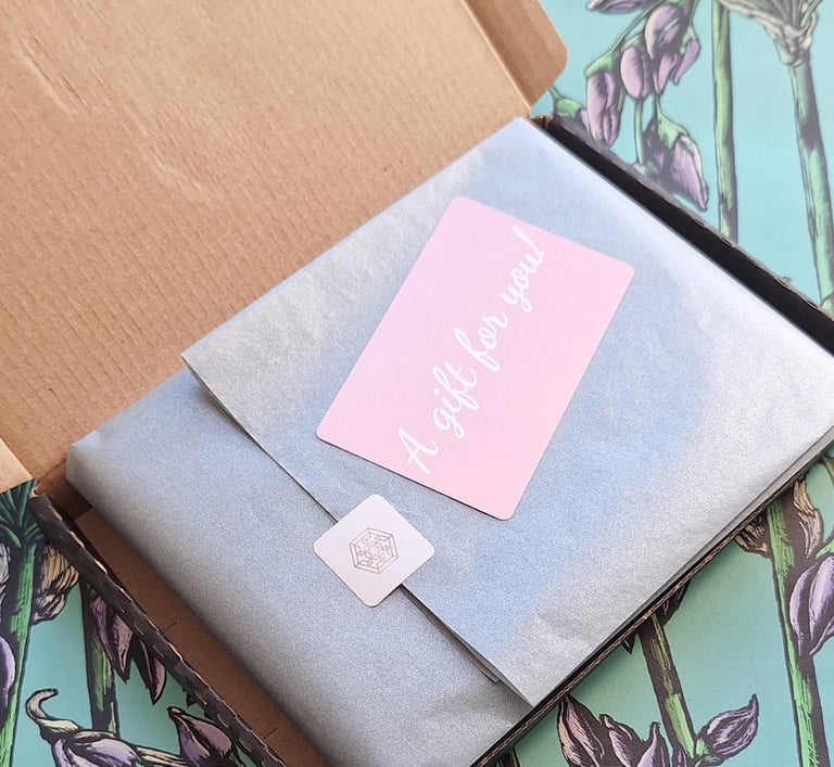 Gift box packaging with grey tissue paper and a pink 'A gift for you' sticker on floral background.