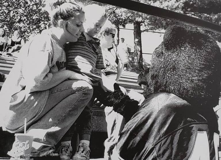 Black and white photo from 1990s of a woman and her child interacting with Topper the Bear