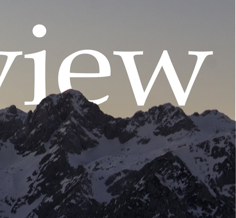 Panoramic mountain view of snow-capped peaks against a dusky twilight sky.