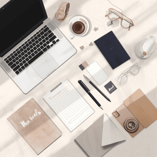 Flat lay of a modern workspace with laptop, coffee, notebooks, and pens on a bright desk.