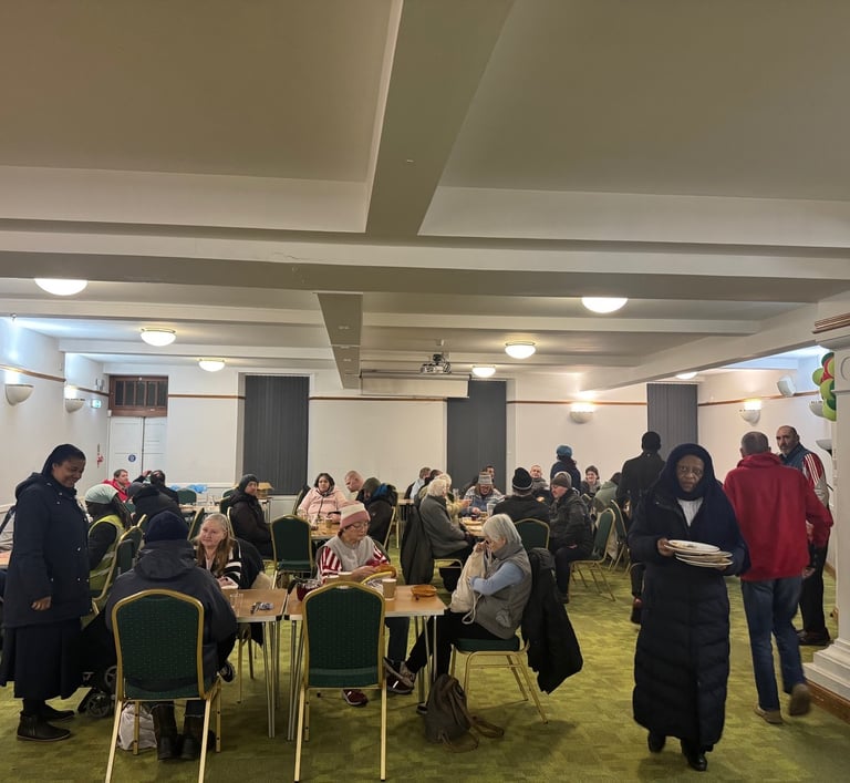 Diverse group of people enjoying a community meal and social gathering in a large hall.
