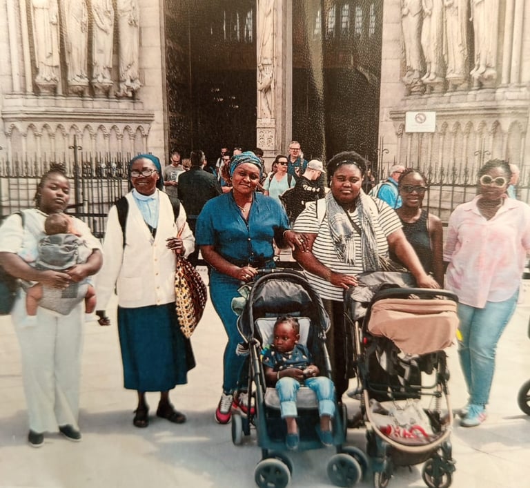 A group of African women and children posing in front of the ornate stone entrance of Notre-Dame de Paris.