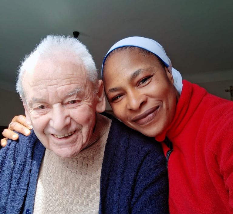 A smiling elderly man and a happy female caregiver in a red jacket posing for a close-up portrait.