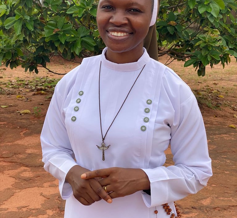 A smiling African Catholic nun wearing a white habit, crucifix necklace, and rosary beads outdoors.
