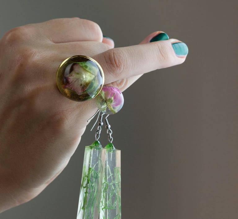 UN llaveros de resina colgando de UN dedo de la Mano de una persona que tiene un anillo con un cuarso Verde y dorado