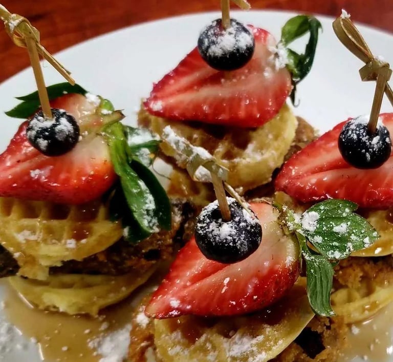 Mini chicken and waffle sliders topped with strawberries, blueberries, and powdered sugar.