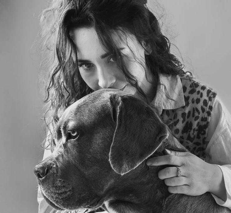 Black and white portrait of a woman with curly hair hugging a large Cane Corso dog.
