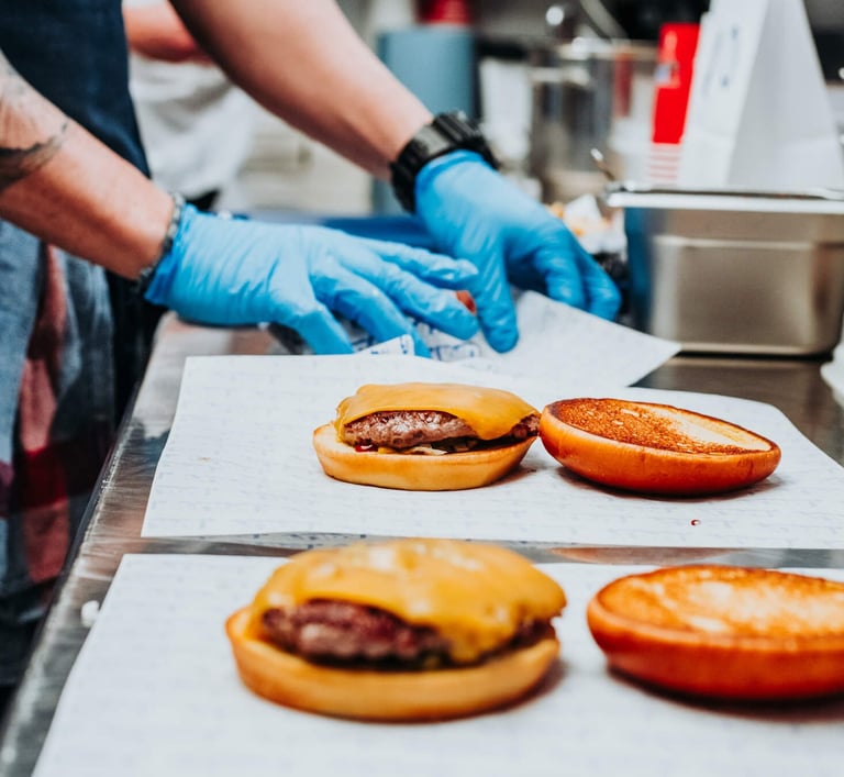 Montaje de hamburguesas en cocina de Flipa con pan tostado y guantes de preparación