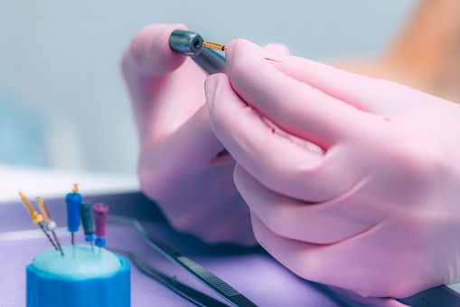 Dentist in pink gloves preparing a dental drill and endodontic files for a root canal procedure.