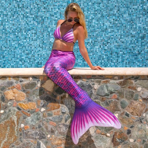 A woman wearing a pink finfun tail. She's sitting on a stone wall, looking down.