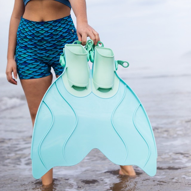 A woman in blue scale-patterned swim shorts. She's holding a light blue monofin.