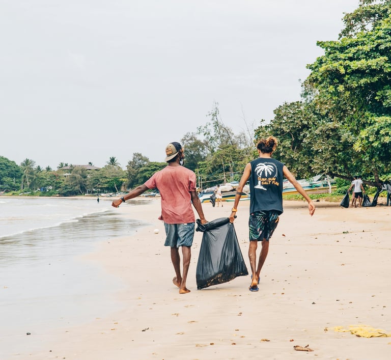 Two men walking down a beach, holding a garbage bag between them.
