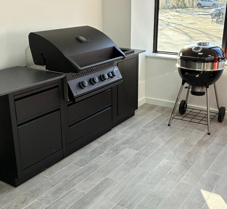 Modern outdoor kitchen featuring a black built-in gas grill and a charcoal kettle grill.