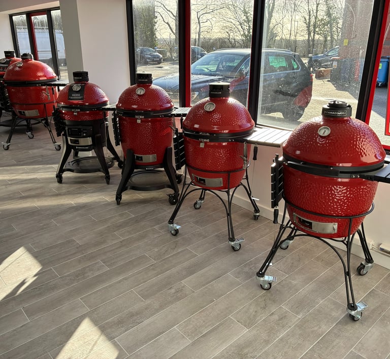 A row of red Kamado Joe ceramic grills on display in a modern outdoor cooking showroom.
