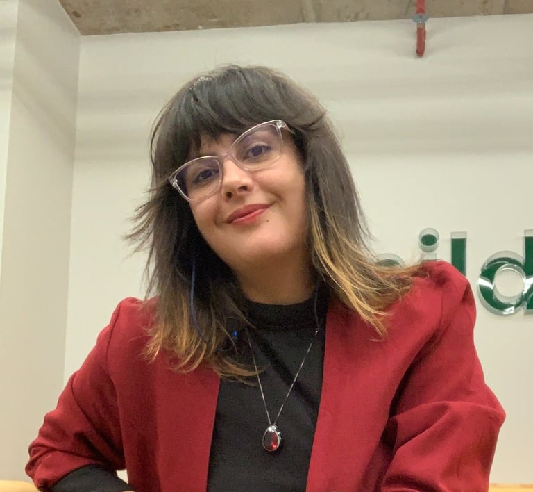 Josi sorrindo e vestida de preto com terno vermelho, cabelos soltos e óculos transparente.