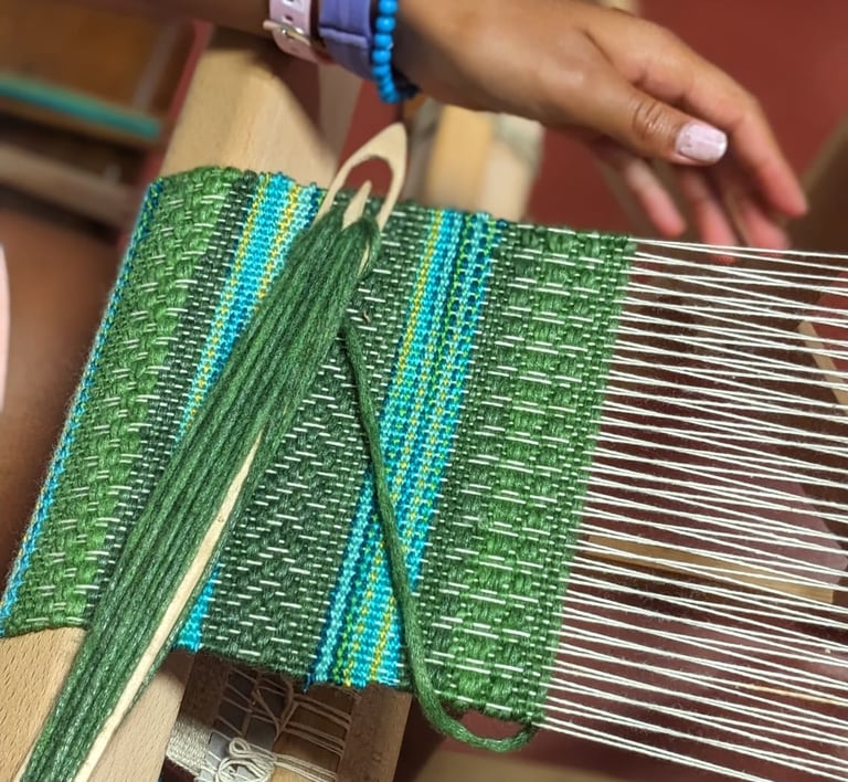 a woman working on a weaving loom with shuttle and green blue threads on a textile in progress