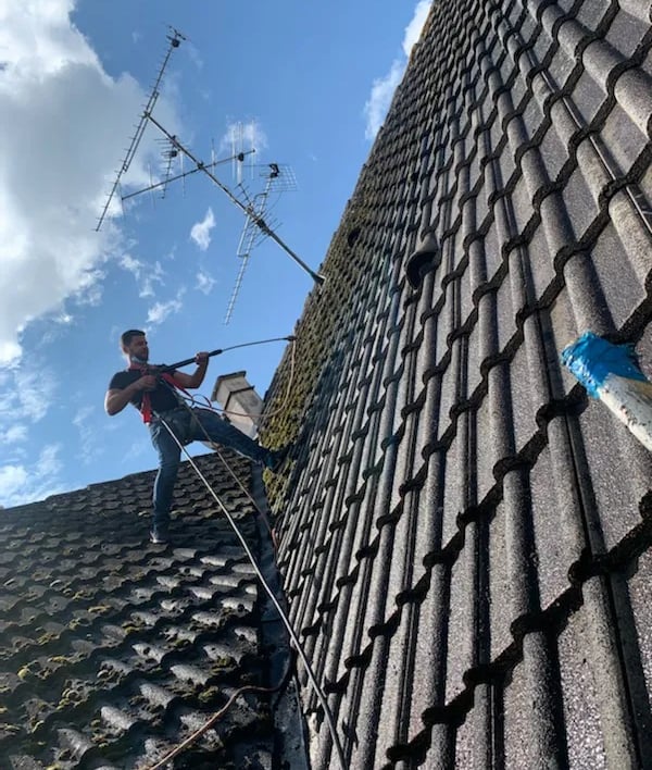 Artisan couvreur en intervention sur une toiture, effectuant un nettoyage haute pression à Belfort, équipé de harnais de sécu