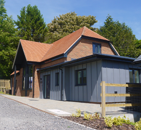 Modern home with red brick walls, grey zinc cladding, and a clay tile roof set against green trees.