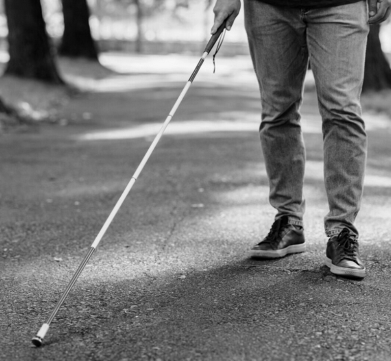 Niewidomy mężczyzna porusza się za pomocą białej laski w ścieżce.