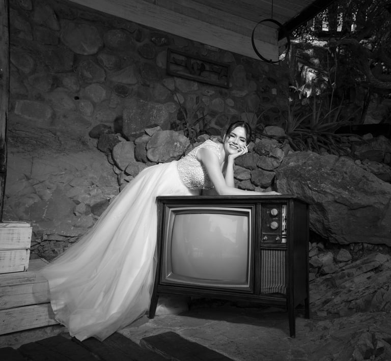 Novia divertida usando un vestido de tul y encaje, recargada en una televisión antigua