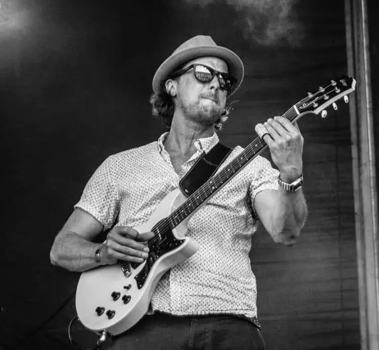 Lead guitarist of Mosaic performing a high-energy country-rock solo at a festival-style wedding