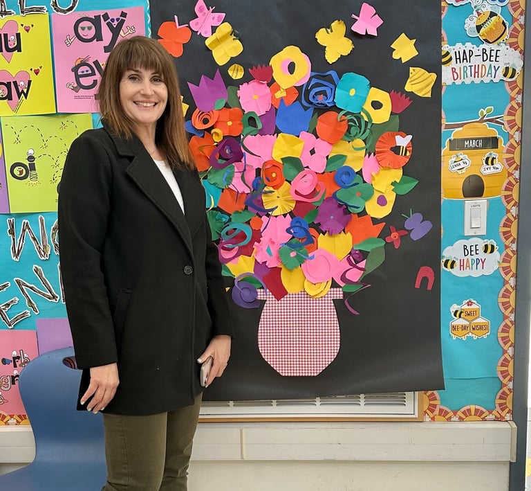 a teacher standing by a collage of paper flowers