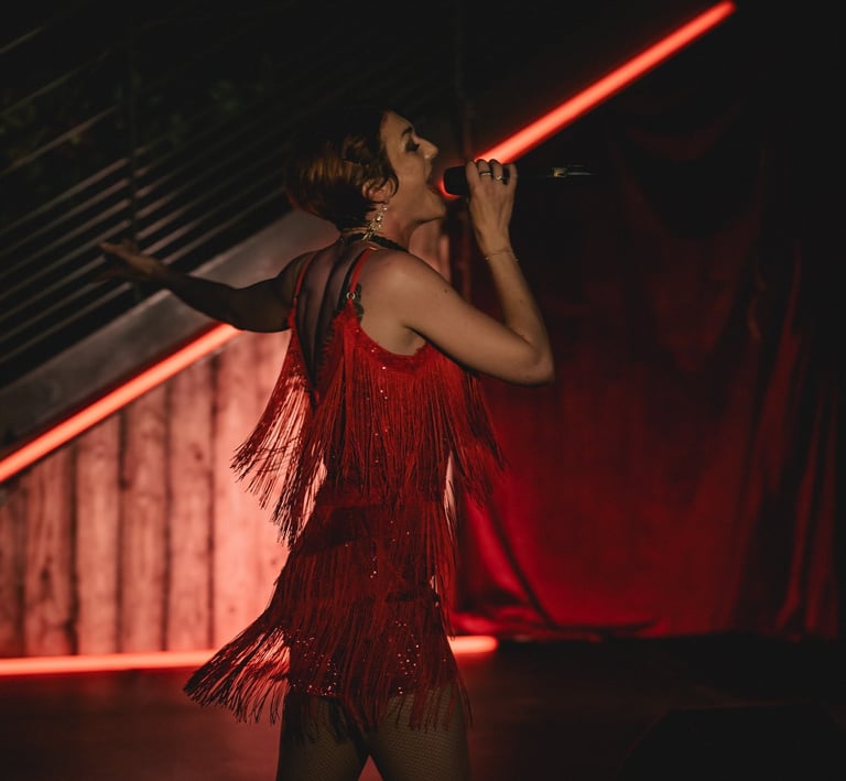 Jessie BaréKa chante sur scène en robe rouge à franges, ambiance cabaret.