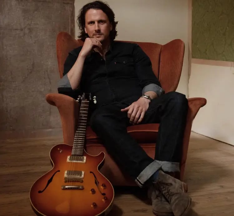 Professional guitarist from Mosaic sitting with a hollow-body electric guitar for an acoustic set