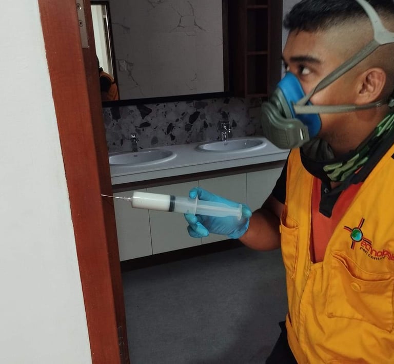 Professional pest control technician wearing a respirator mask applying termite gel treatment into a door frame.
