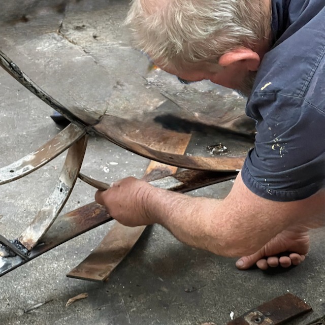 A skilled metalworker bends and shapes rusty metal strips for a custom sculpture project.