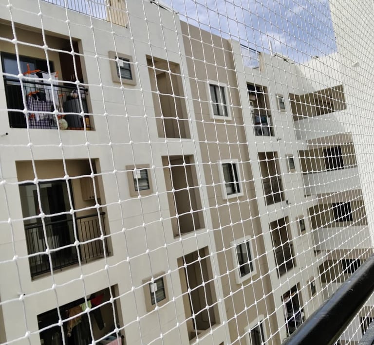 Wide shot of a high-rise balcony fully covered with a transparent safety net against a clear sky.