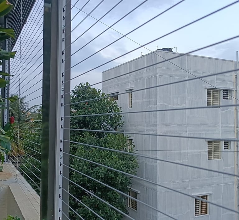Side perspective of invisible grills installed on a high-rise apartment window overlooking greenery.