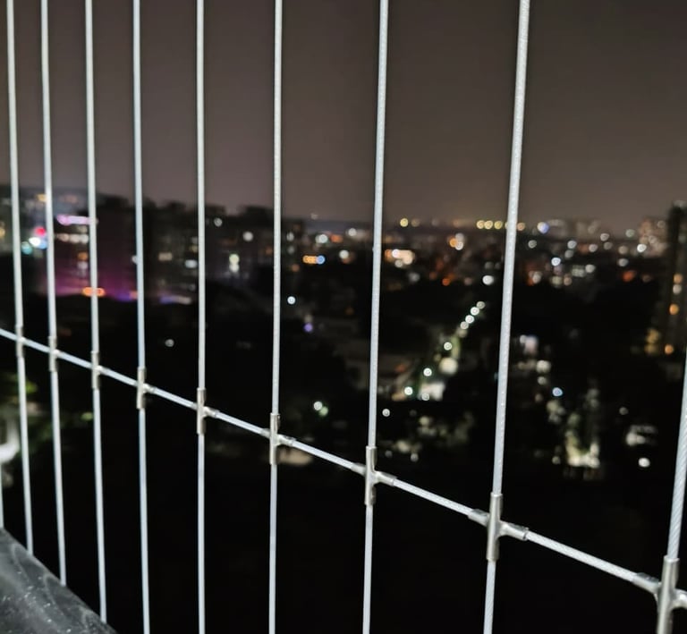 Technician carefully fitting fine mesh safety net along a balcony edge to ensure child safety.