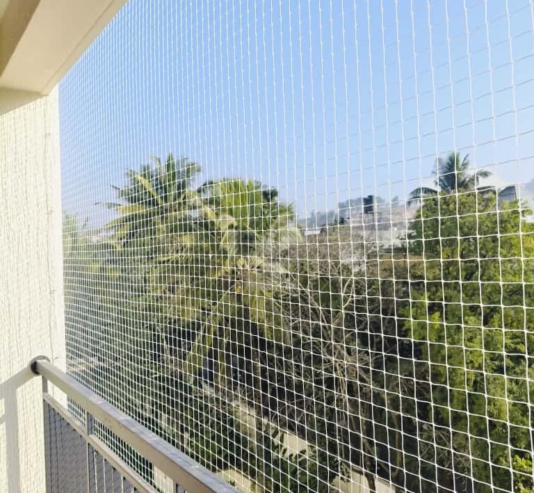 Wide shot of a balcony fully covered with safety netting overlooking a green neighborhood in Adyar.