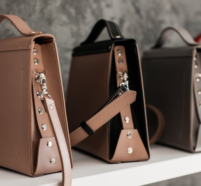 Collection of stylish leather satchel handbags with metal stud details displayed on a shelf.