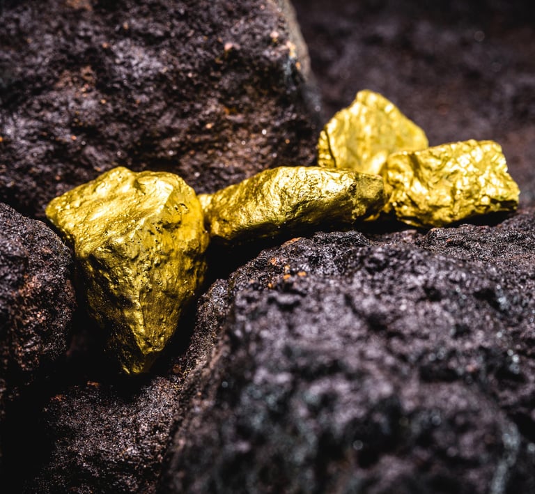 Natural raw gold nuggets resting on dark volcanic rock minerals in a close-up shot.