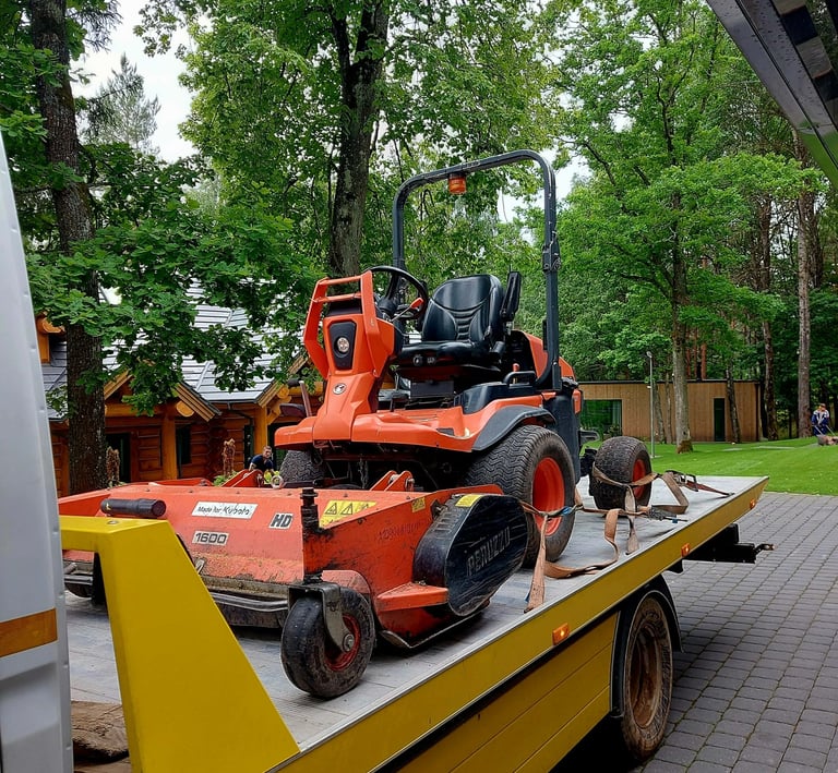 Orange Kubota ride-on lawn mower secured on a yellow flatbed truck for professional landscaping transport.