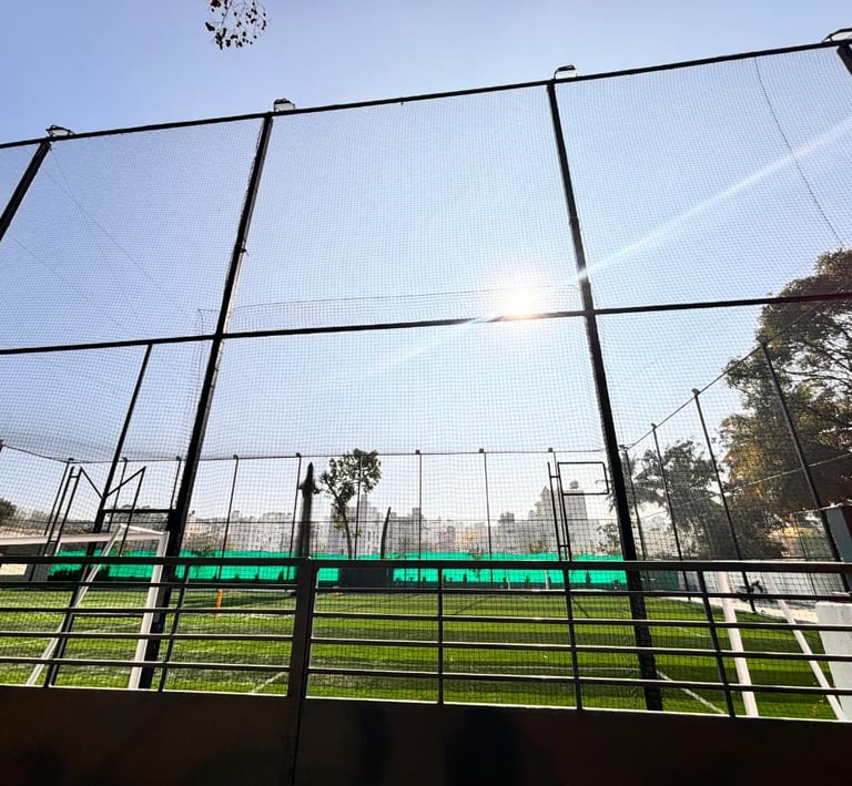 Wide shot of a sports practice net enclosing a cricket pitch under bright sunlight.
