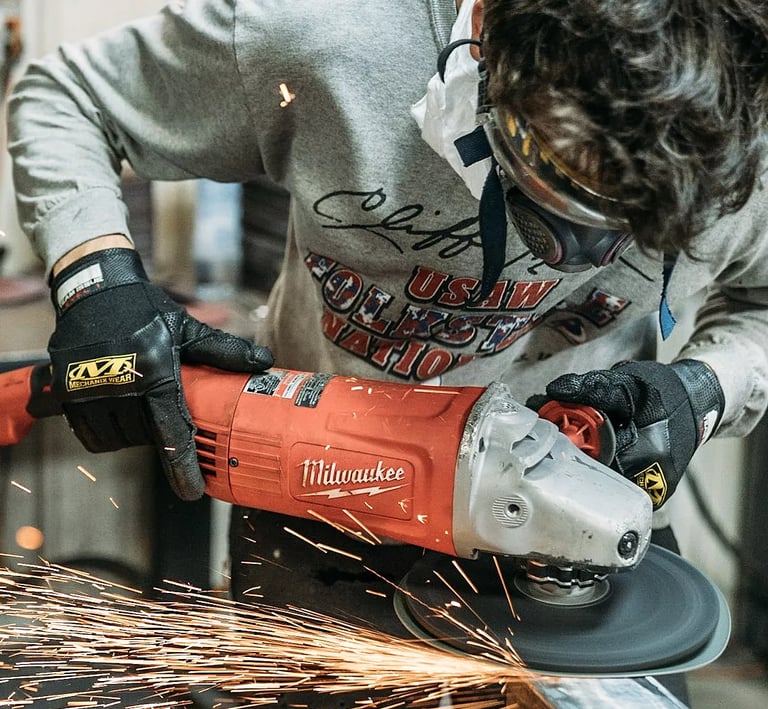 A metalworker uses a red Milwaukee angle grinder to smooth steel, creating bright orange sparks.