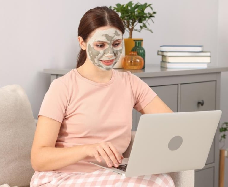 Una mujer lleva una mascarilla facial mientras usa su ordenador portátil y se relaja