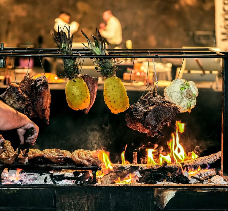 Chef asando chorizo argentino y carnes colgadas con piñas sobre un asador de leña al fuego abierto.