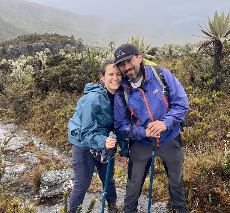 A smiling couple hiking with trekking poles on a foggy trail in the paramo mountains.