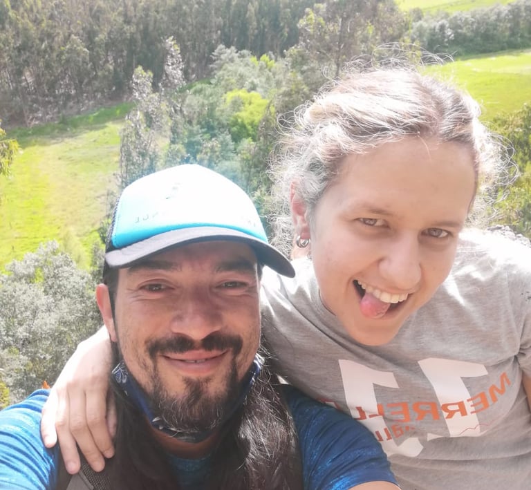 Smiling couple taking a selfie while hiking in a lush green valley with forest views.