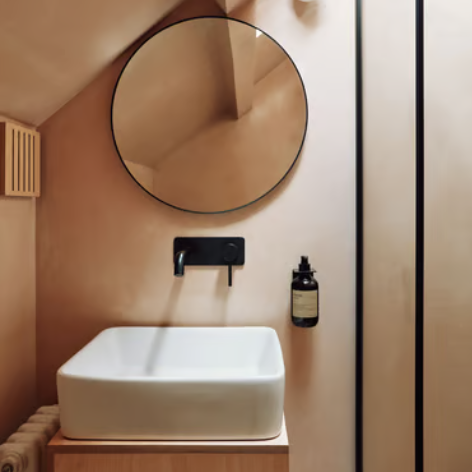 Modern bathroom vanity featuring a white vessel sink, matte black faucet, and a round wall mirror.