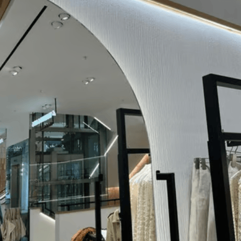 Modern luxury clothing store interior featuring a minimalist textured archway and designer apparel on black display racks.